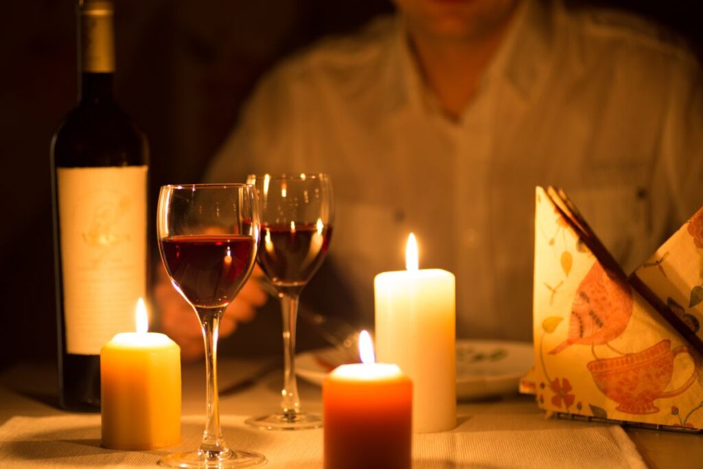 Garrafa de vinho tinto e duas taças cheias, iluminadas por três velas, em um jantar à luz de velas, sugerindo romance e intimidade.