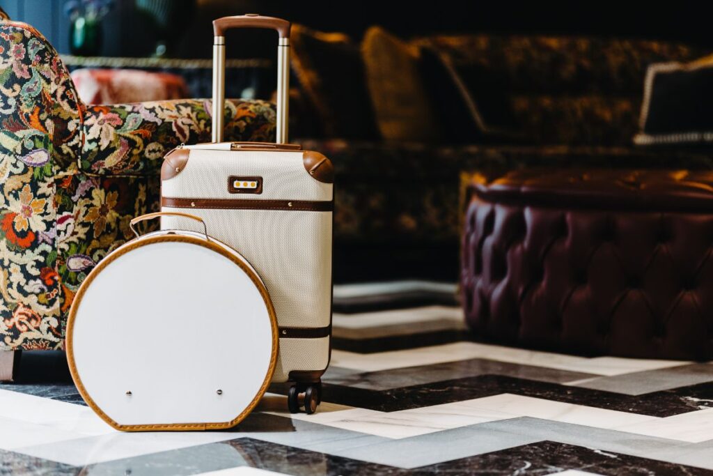 Duas malas de viagem, uma delas com rodas, em um lobby elegante de hotel, prontas para o check-in nas hospedagens.