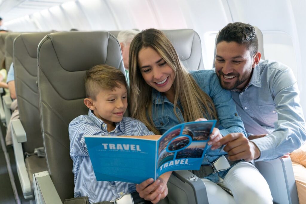 Família em um avião, com pais e filho lendo um guia de viagens econômicas.