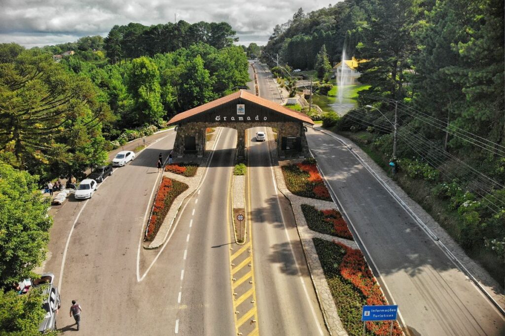 Vista aérea do pórtico de entrada de Gramado cercado por jardins floridos e muito verde na Serra Gaúcha