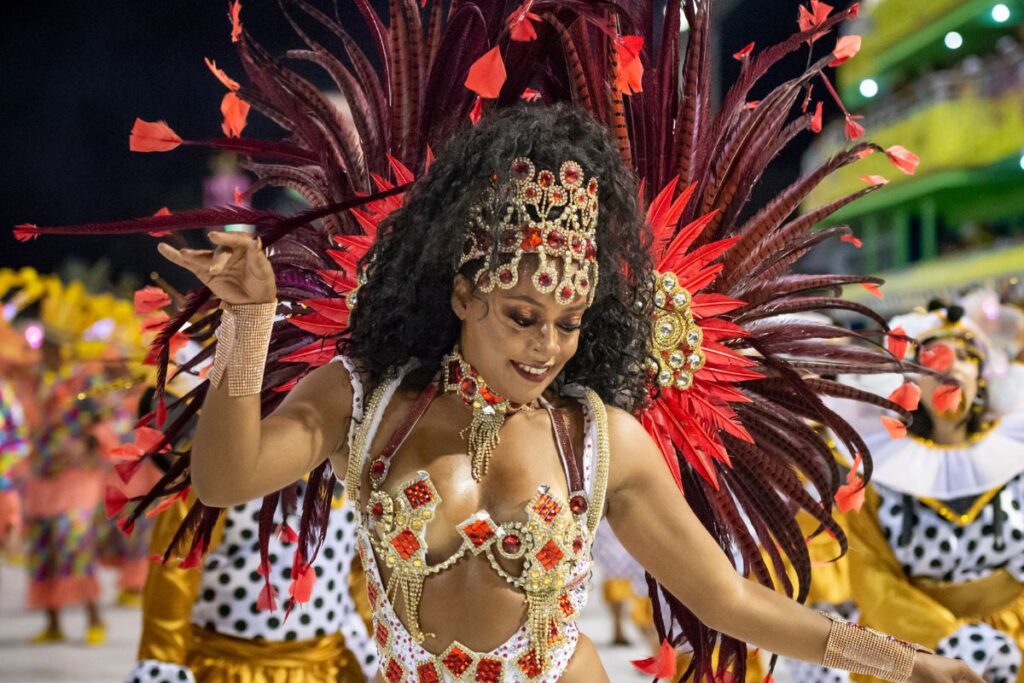 Porta-bandeira com fantasia elaborada de plumas vermelhas desfilando no Carnaval do Rio de Janeiro, a festa mais incrível do planeta