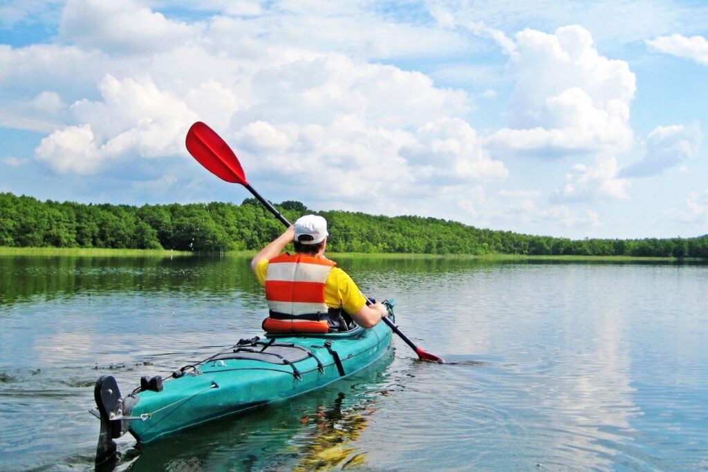 Canoísta praticando caiaque em lago tranquilo cercado por floresta, esporte aquático contemplativo descoberto viajando