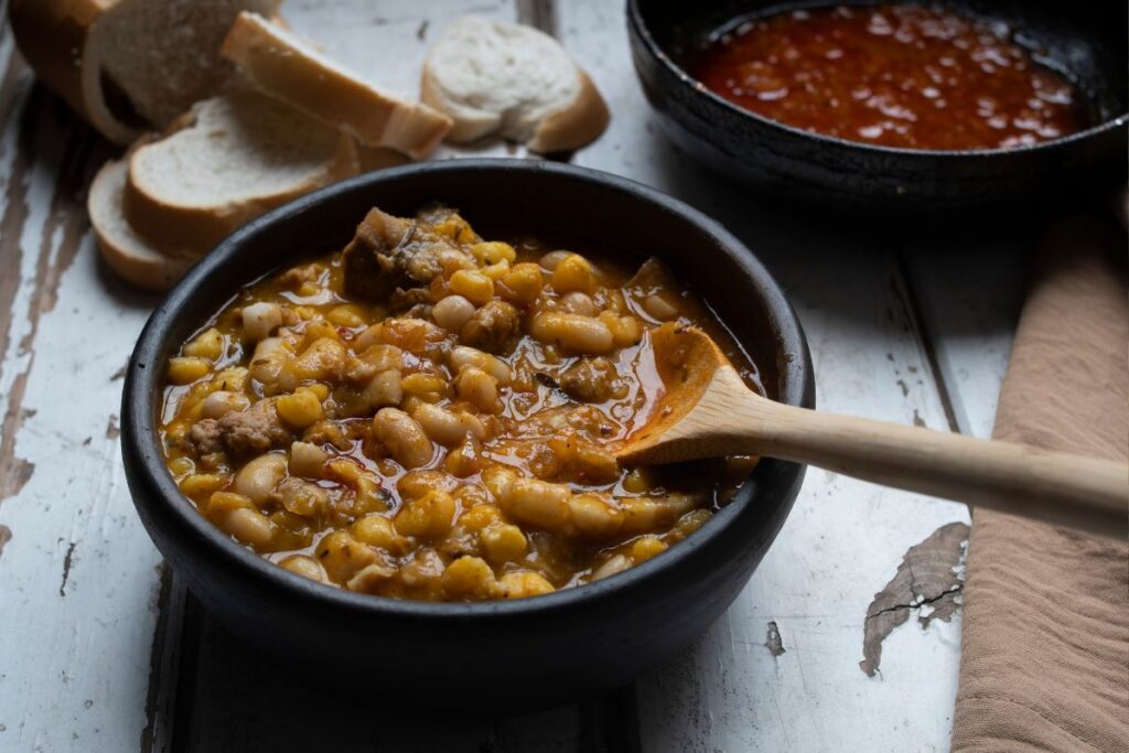 Uma tigela de guiso de lentejas e milho com pão fatiado ao lado.