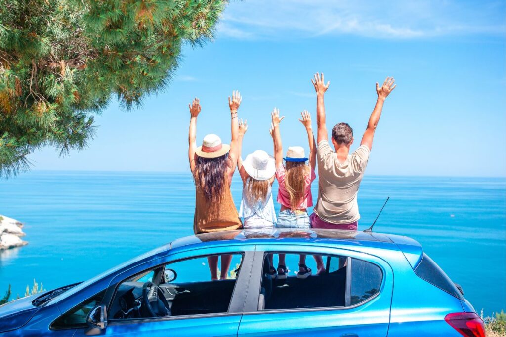 Família de costas acenando em cima de um carro com o mar de fundo.