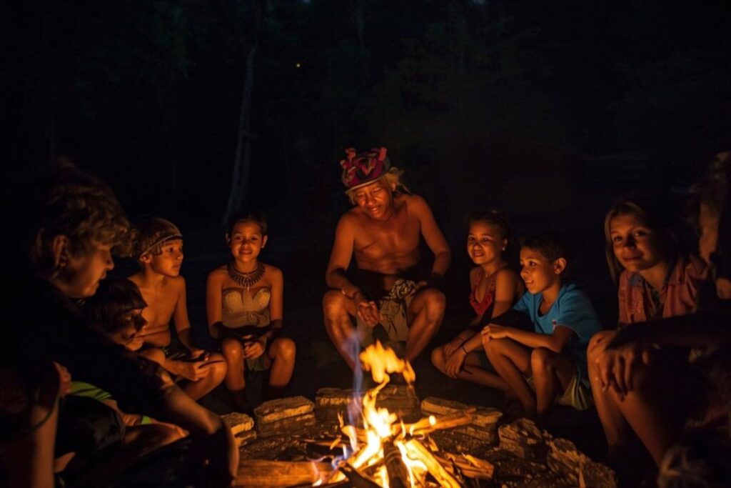 Povos indígenas reunidos ao redor da fogueira na Floresta Amazônica, compartilhando histórias, lendas e saberes ancestrais sob a luz do fogo.