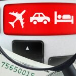 Lupa sobre teclado de computador com ícones de avião, carro e cama, simbolizando a busca por hospedagens e viagens.