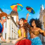 Três mulheres fantasiadas celebrando o Carnaval do Rio de Janeiro nas ruas do centro histórico com sombrinhas coloridas