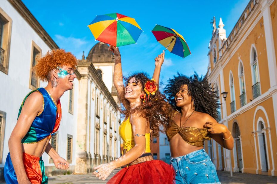 Três mulheres fantasiadas celebrando o Carnaval do Rio de Janeiro nas ruas do centro histórico com sombrinhas coloridas