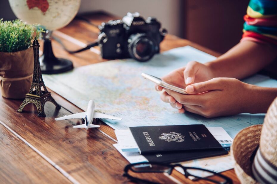 Pessoa organizando viagem com celular, passaporte, mapa e câmera, indicando a pesquisa de destinos para um roteiro de viagem que realmente funcione.
