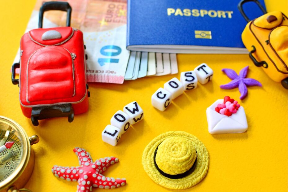 Vários itens de viagem, incluindo um passaporte, uma mala pequena, uma bússola e notas de euro, com blocos de letras formando a frase "LOW COST".