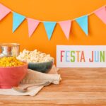 Mesa decorada com bandeirinhas coloridas, milho cozido, pipoca e placa escrita Festa Junina representando as tradicionais celebrações juninas brasileiras