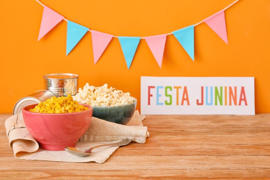 Mesa decorada com bandeirinhas coloridas, milho cozido, pipoca e placa escrita Festa Junina representando as tradicionais celebrações juninas brasileiras
